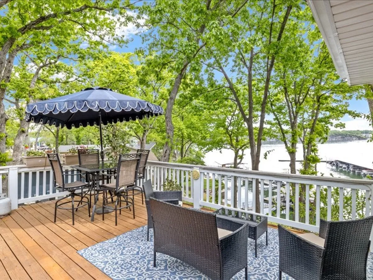 An inviting outdoor dining area featuring a table and blue umbrella, set against a lush backdrop with clear views of the water. The space is surrounded by greenery, evoking relaxation and a close connection to nature.