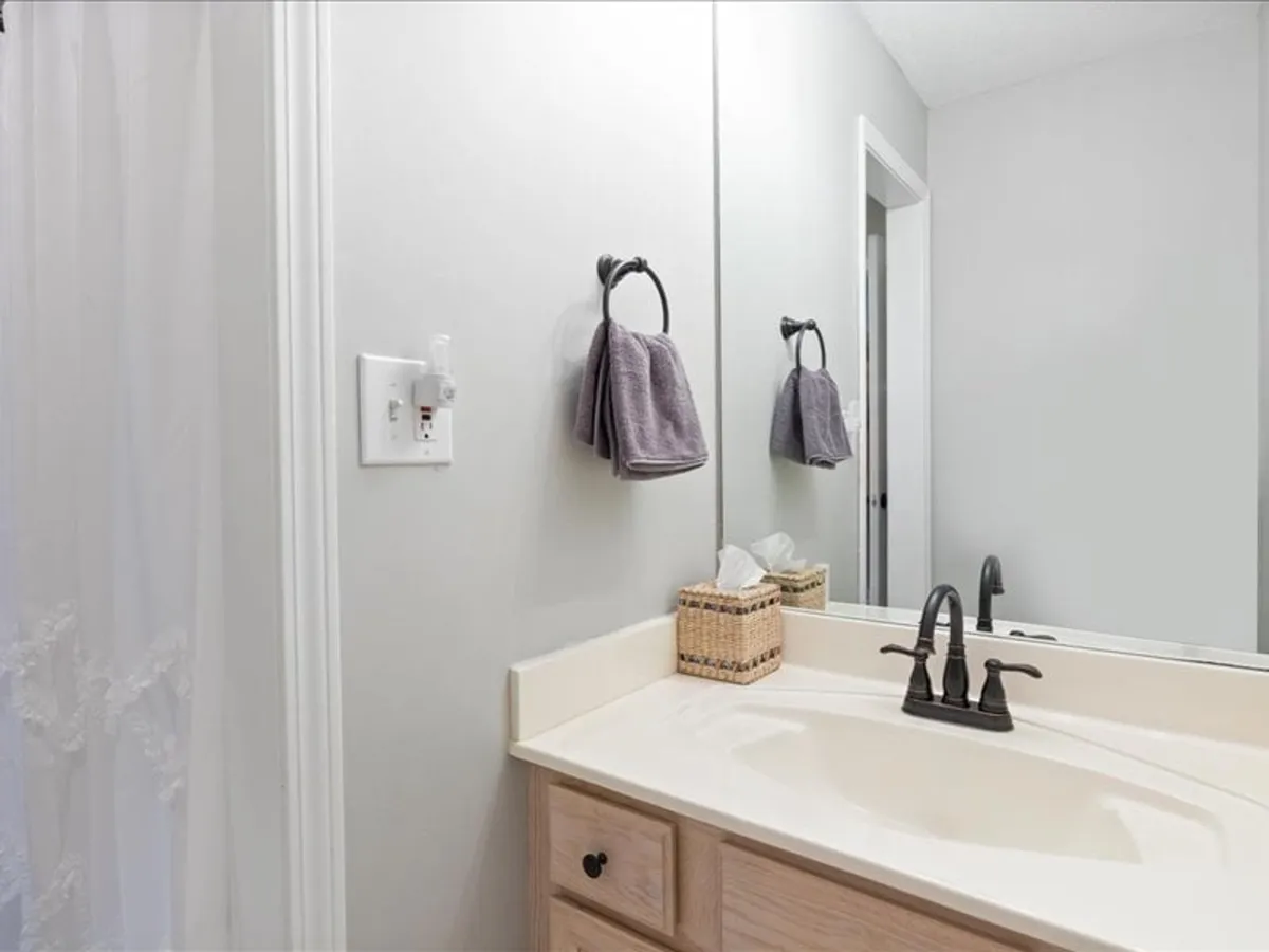 A bright, inviting bathroom with a modern sink and faucets, a round mirror, fresh towels, and a woven basket. The space is clean, serene, and equipped for comfort and self-care.
