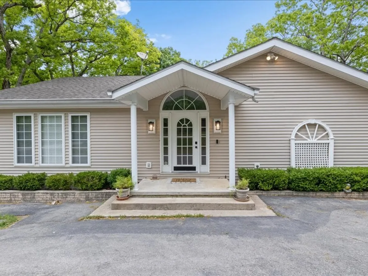 The image showcases the front entrance of the lake home, framed by neatly landscaped shrubs and symmetrical architecture. The inviting pathway leads to a welcoming front door, suggesting both privacy and a sense of arrival. The setting exudes an atmosphere perfect for gatherings or tranquil mornings.