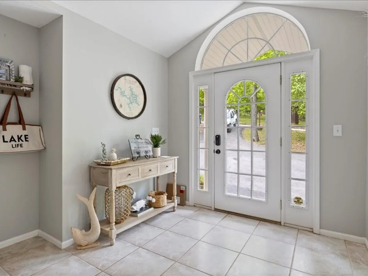 This image features the front door entryway of the home, complete with a console table, a 'lake life' bag, and a wall map. The styling is inviting, signaling arrival and first impressions, and the entry area is tidy and thoughtfully decorated.