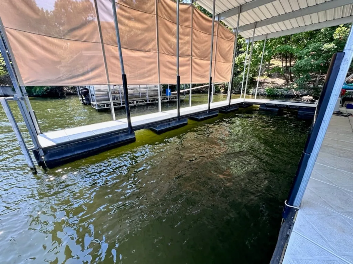 A dock shaded by a canopy extends over sparkling water, framed by lush greenery. The scene is peaceful and encourages relaxation or an early morning fishing session, with the dock easily accessible for activities like fishing or boating.