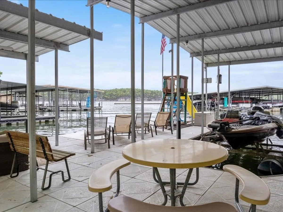 A lively exterior scene displaying a table and chairs for outdoor gatherings, boat docks primed for water activities, and a visible playground structure—all bathed in the warm glow of sunset over the lake.