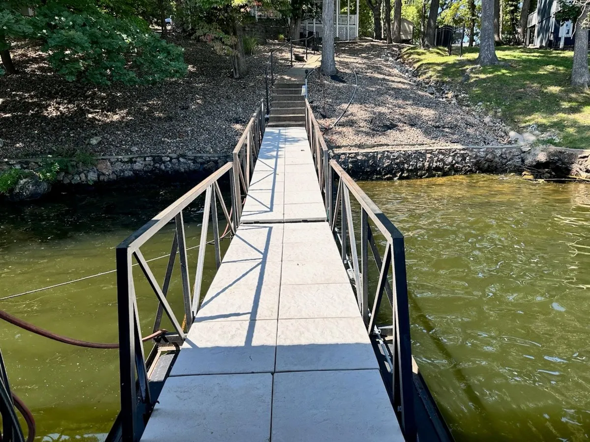 A wooden dock extends out onto a calm lake, bordered by tall trees. The setting is serene and untouched, inviting families to take morning walks, fish, or simply enjoy the quiet beauty of the water and surrounding nature.